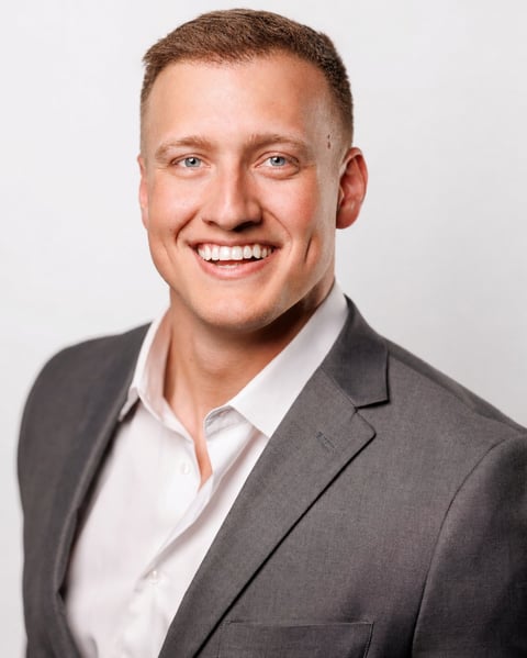 Professional headshot of a smiling man in a gray blazer and white shirt against a light background